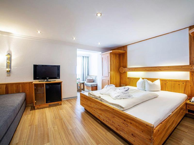 Helles Schlafzimmer mit Holzmöbeln, großem Bett, TV, Sofa und Holzfußboden.