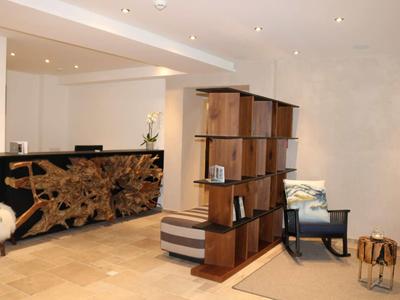 Modern hotel lobby with wooden reception desk, partition shelf, armchairs, and warm inviting design.
