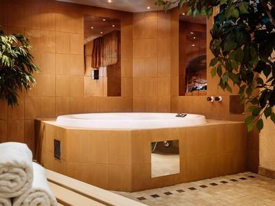 Luxurious bathtub in warm wood-paneled room with plants and towels.