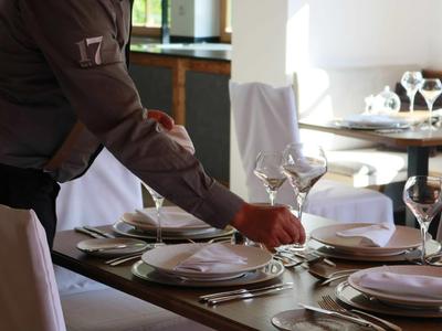 Waiter sets table with white plates and wine glasses in elegant restaurant.