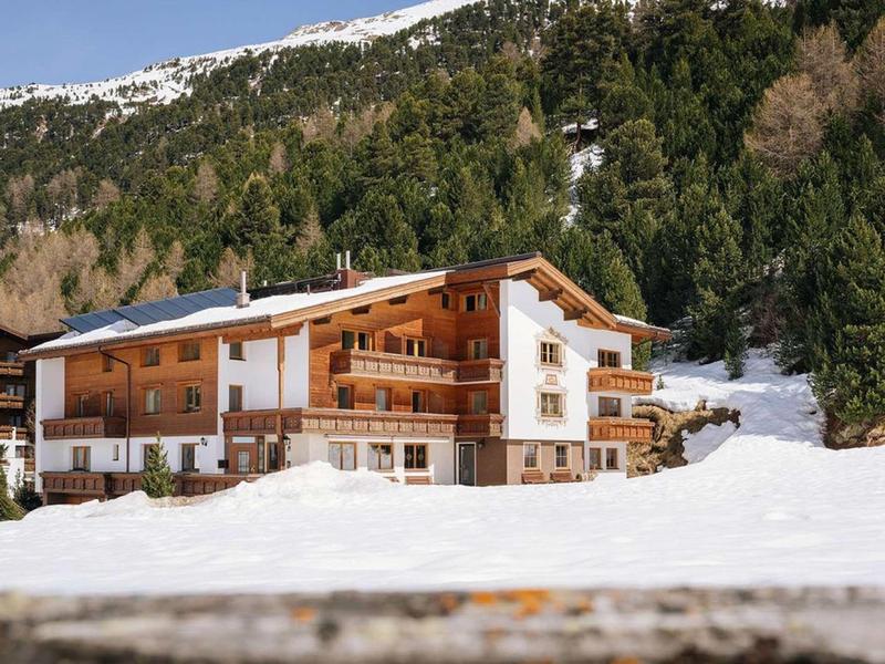 Large chalet in winter with snow and forested mountains in the background.