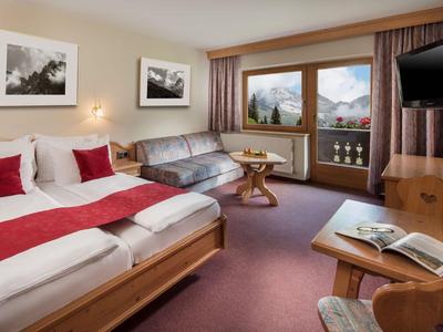 Pohodlný hotelový pokoj s manželskou postelí, pohovkou, balkonem a výhledem na hory.