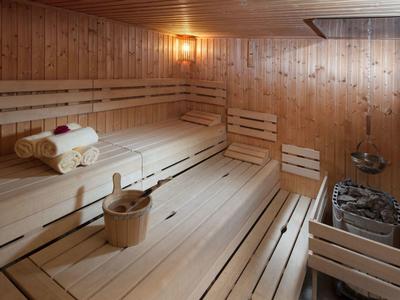 Holzsauna mit Sitzbänken, Handtüchern, Holzeimer und Saunaofen, warmes Licht, rechteckiges Fenster.