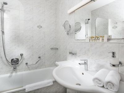 Světlá koupelna s bílou vanou, umyvadlem a srolovanými ručníky.