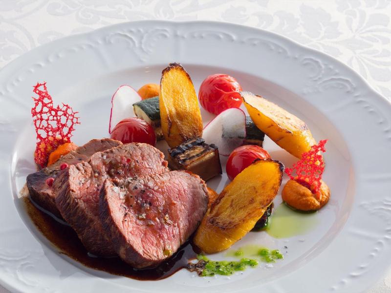 Anrichten von rosa gebratenem Fleisch mit buntem Gemüse und Dekoration auf weißem Teller.