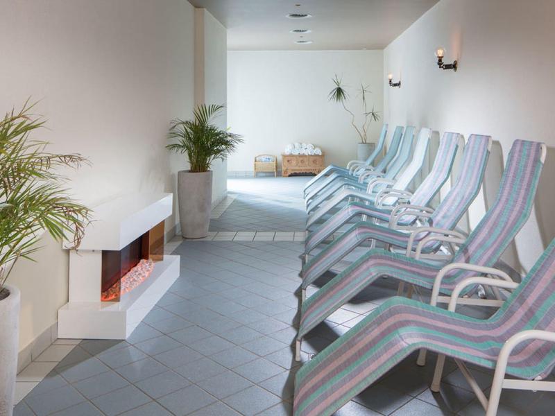 Entspannungsraum mit Liegestühlen, Pflanzen und modernem Kamin in hellem, ruhigem Ambiente.