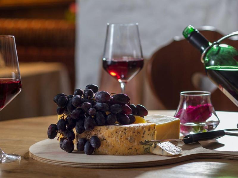 Tisch mit rotem Wein, Trauben, Käse und Kerze in gemütlicher Atmosphäre.