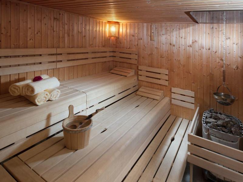 Holzsauna mit Sitzbänken, Handtüchern, Holzeimer und Saunaofen, warmes Licht, rechteckiges Fenster.