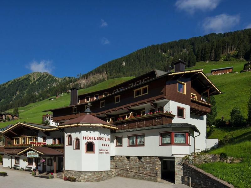 Altes Gasthaus vor grünen Hügeln unter blauem Himmel mit wenigen weißen Wolken.