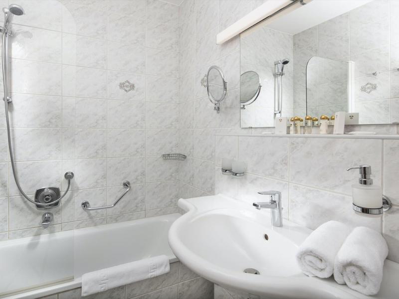 Helles Badezimmer mit weißer Badewanne, großem Waschbecken, Spiegel und weißen Handtüchern.