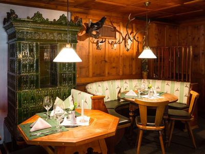 Gemütliche Holzecke mit Sitzbank, Stühlen, gedeckten Tischen und grünem Kachelofen im Raum.