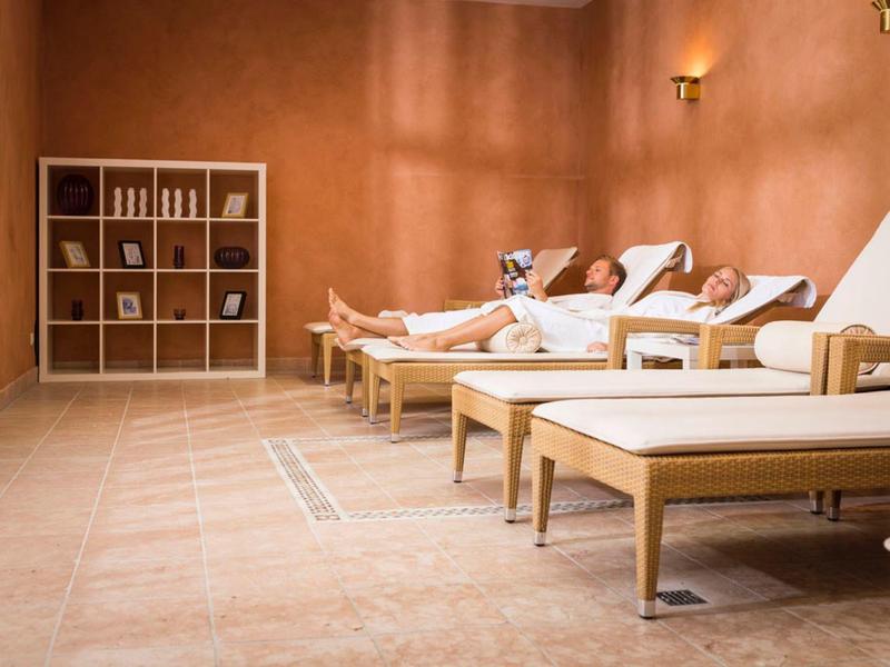 Ruheraum mit weißen Liegen und warmen Wandfarben, weiches Licht und Regale mit Dekoration.