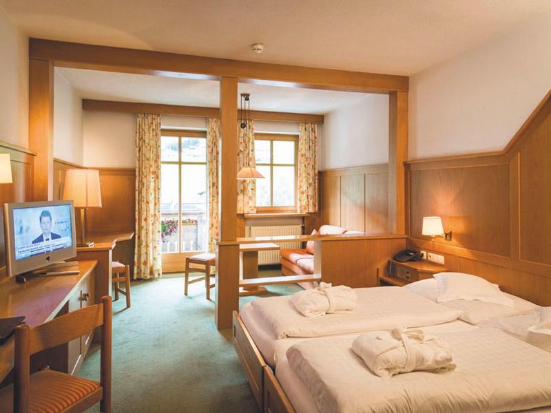 Gemütliches Hotelzimmer mit Doppelbett, Holzvertäfelung, Schreibtisch, Fernseher und Balkon.