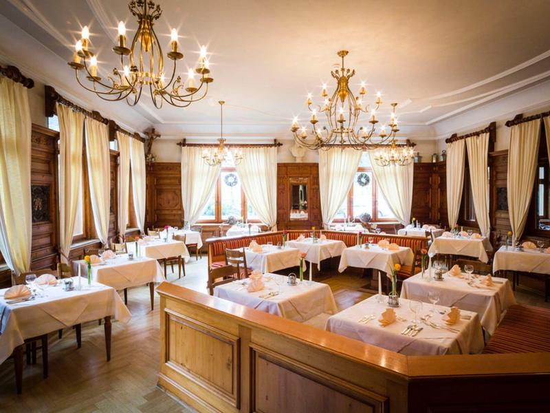 Festlich gedeckter Speisesaal mit Kronleuchtern, hellen Vorhängen und elegantem Holzmobiliar.