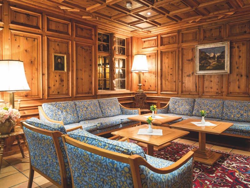 Gemütliches Wohnzimmer mit holzverkleideten Wänden, blauen gemusterten Sofas, zwei Lampen und Teppich.