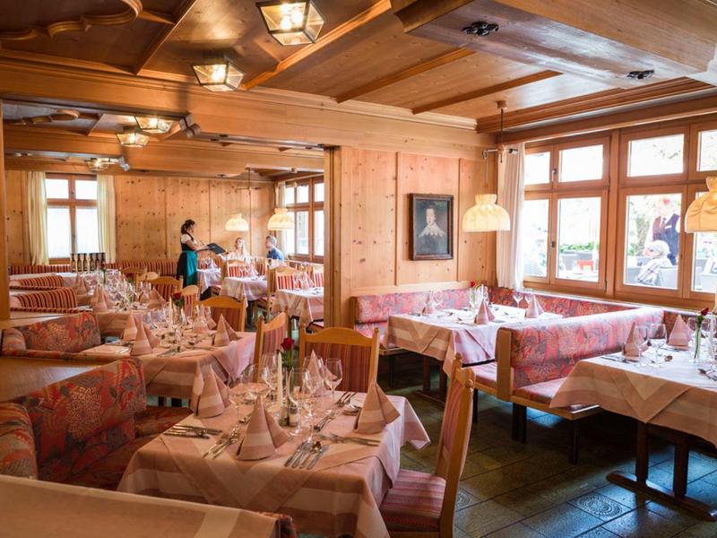 Gemütliches Restaurant mit Holzwänden, gedeckten Tischen und großen Fenstern am Tag.