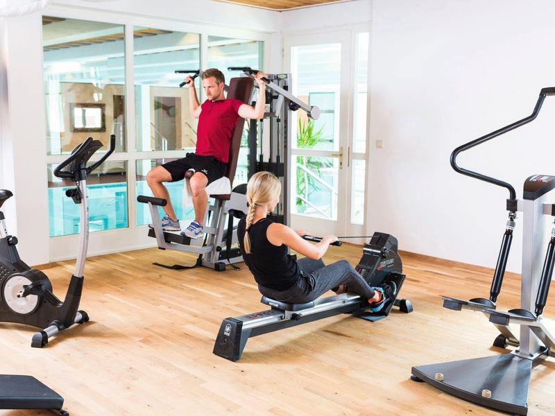 Fitnessraum mit verschiedenen Trainingsgeräten und zwei Personen beim Kraft- und Rudertraining.
