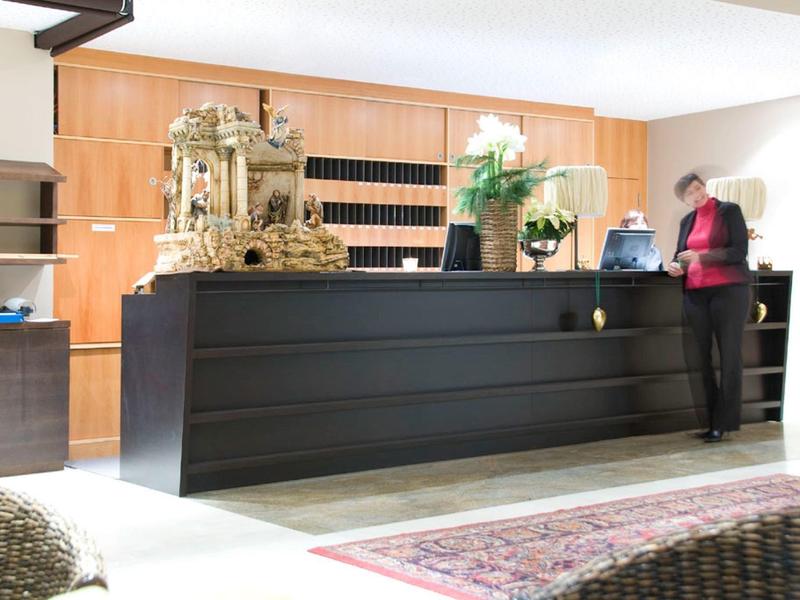 Moderner Empfang mit dunkelgrauem Tresen, goldenem Dekor, Pflanzen und Teppich auf hellem Boden.