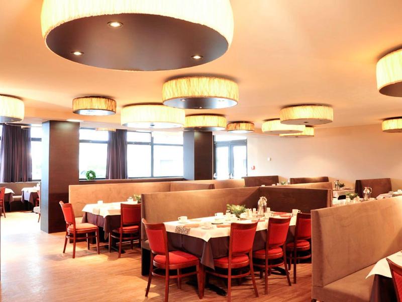 Helles Restaurant mit roten Stühlen, gedeckten Tischen und großen runden Deckenleuchten.