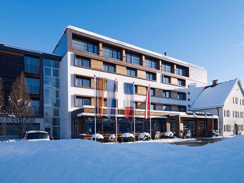 Modernes Hotelgebäude mit fünf Stockwerken, im Vordergrund liegt eine dicke Schneeschicht.