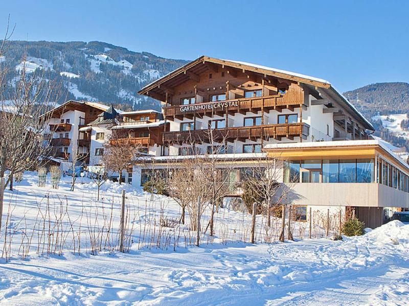 Großes Holzhaus mit Balkonen in verschneiter Winterlandschaft vor bewaldeten Bergen.