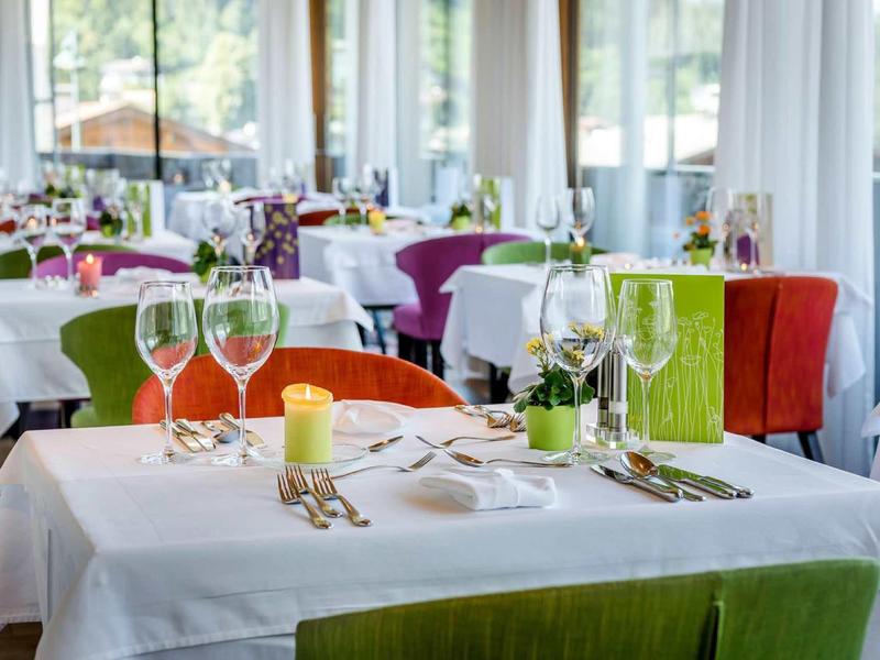 Restaurant mit weiß gedeckten Tischen, bunten Stühlen und geschmackvoller Tischdekoration bei Tageslicht.