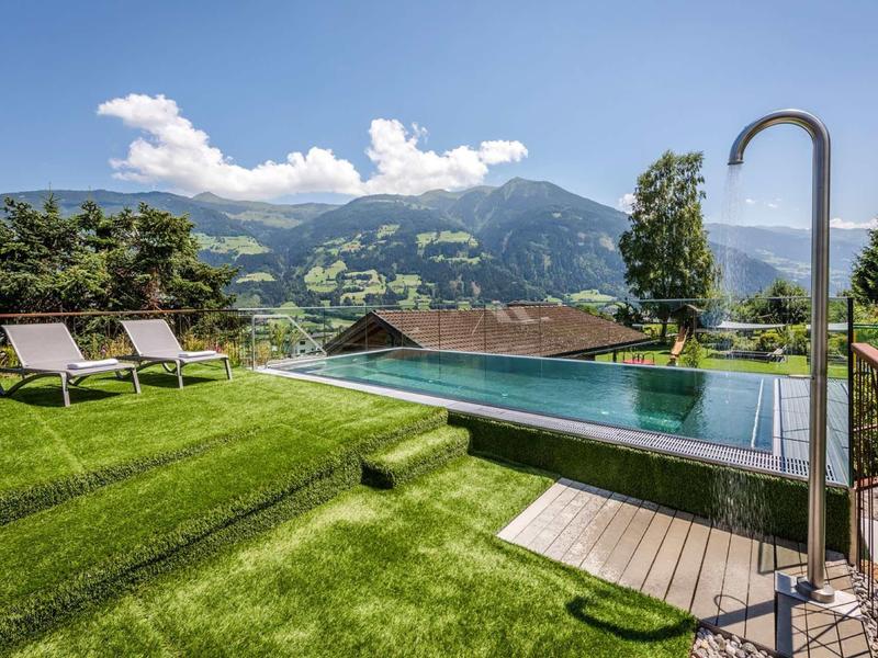 Schwimmbad mit Liegestühlen und Bergblick, grüner Rasen und blauer Himmel.
