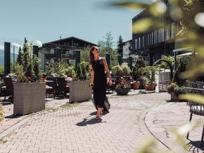 Woman in black dress walking on paved path between hotel buildings on sunny day.