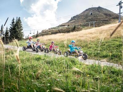 Several children ride on a wild mountain cart track in a mountain landscape.