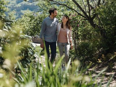 Paar spaziert Hand in Hand auf einem schattigen Waldweg im Grünen.