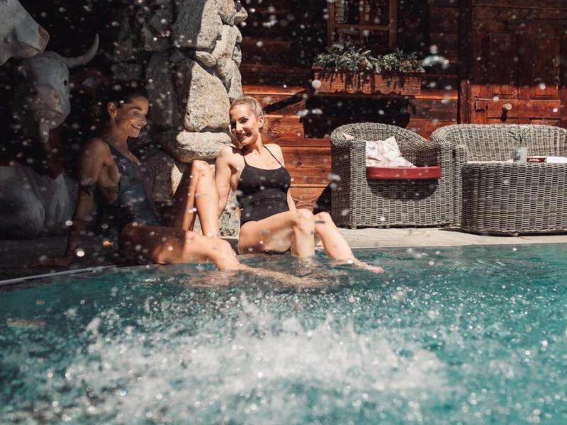 Zwei Frauen entspannen sich am Pool und genießen das spritzende Wasser.