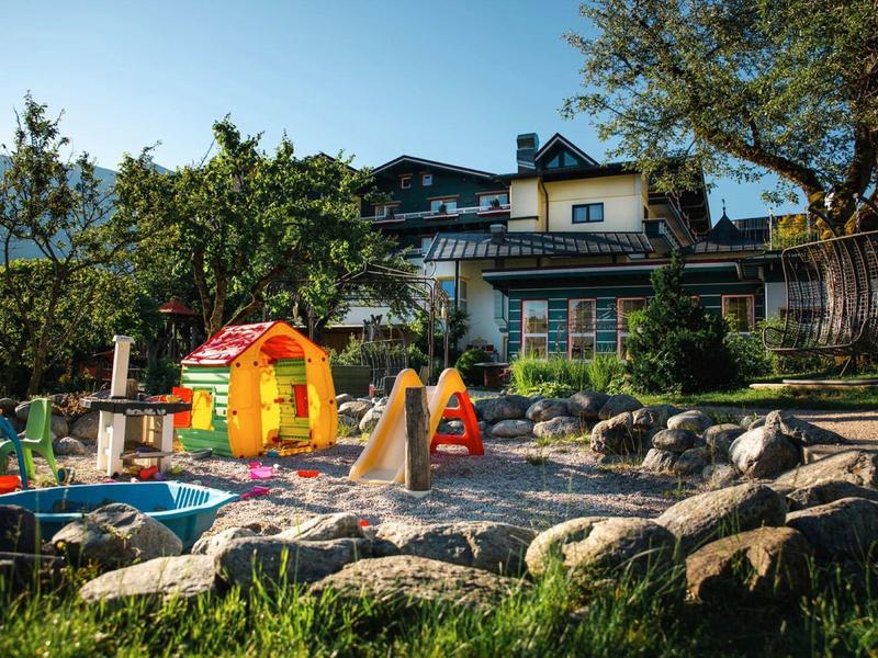 Ein Garten mit tollem Kinderspielplatz vor einem großen Haus in sonniger Landschaft.