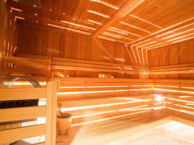 Helle Sauna mit Holzlatten, Bänken und Licht, das durch schmale Spalten fällt.