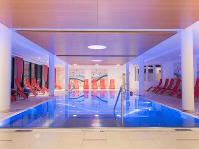 Moderne binnenzwembad met rode ligstoelen en rustgevende verlichting in een wellnessruimte.