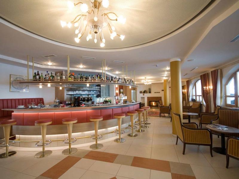 Elegante Bar mit rundem roten Tresen, goldenen Hockern, Pendelleuchten und bequemen Sesseln.