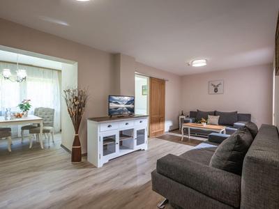 Nowoczesny salon z dwiema sofami, telewizorem i widokiem na przylegającą jadalnię.