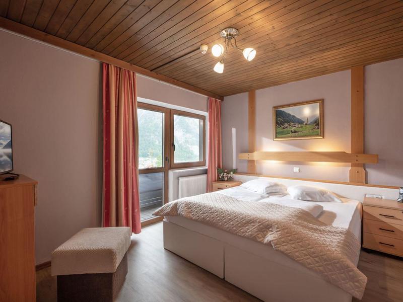 Gemütliches Schlafzimmer mit Doppelbett, Holzmöbeln, roten Vorhängen und großem Fenster.