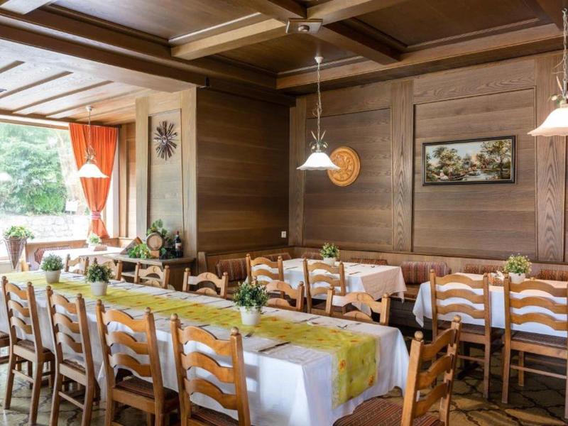 Gemütlicher Holzraum mit langer gedeckter Tafel, Stühlen und großen Fenstern mit orangen Vorhängen.