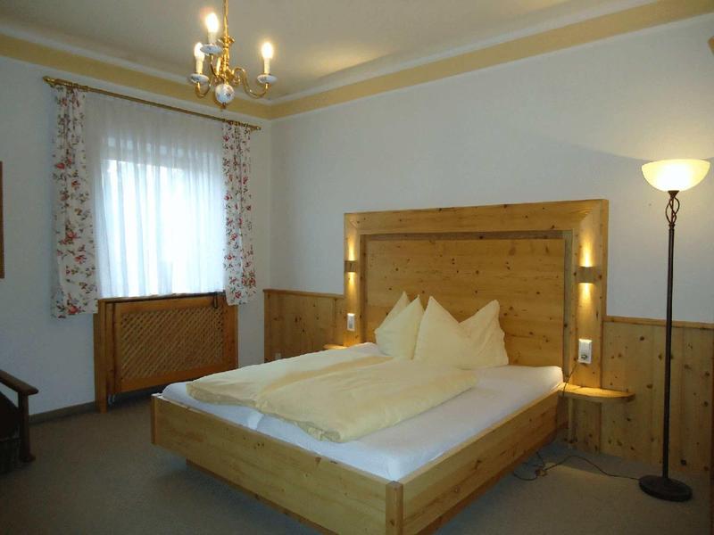 Gemütliches Schlafzimmer mit hellem Holzbett, weißen Decken und Vorhängen, Stehlampe und Kronleuchter.