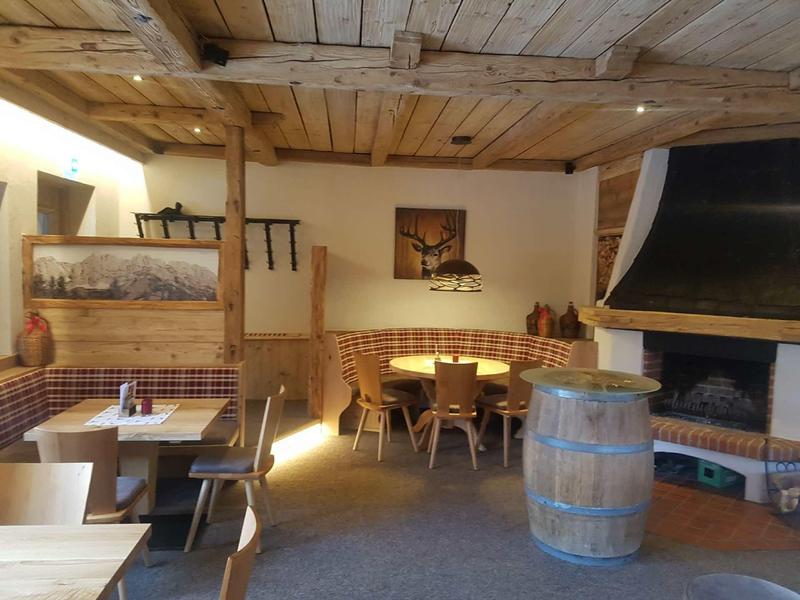 Gemütlicher, rustikaler Gastraum mit Holzbalken, Eckbank, Holztischen und einem Kamin mit Fass.