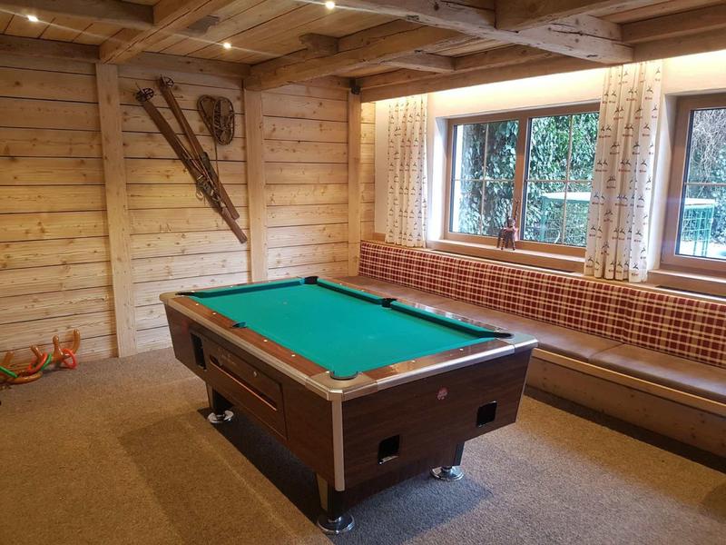 Gemütlicher Raum mit grünem Billardtisch, Holzwänden, Fensterbank und Ski-Dekor an der Wand.