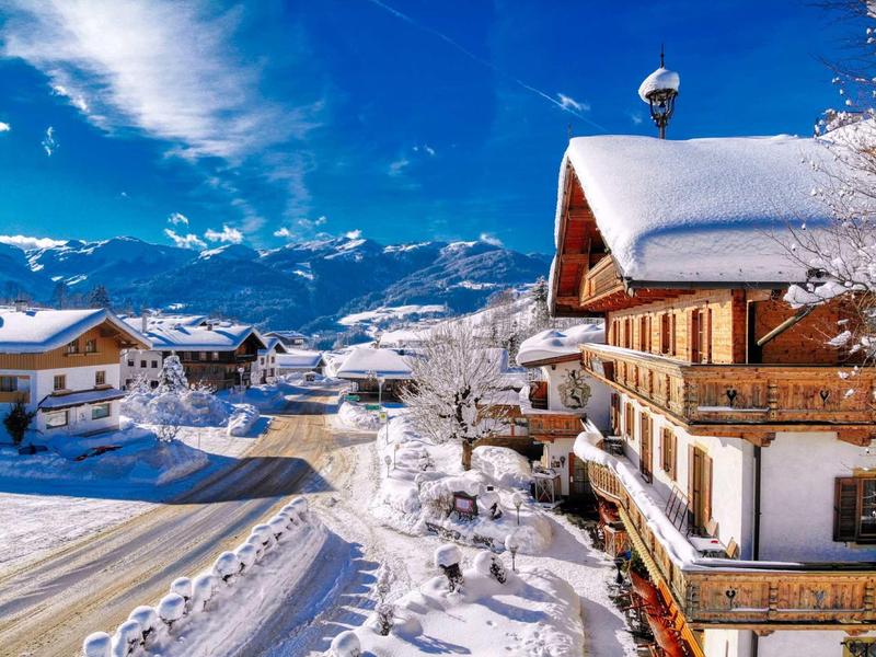 Winterlandschaft mit schneebedeckten Chalets und Bergen unter blauem Himmel.