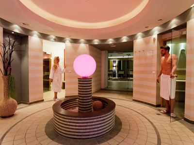 Runder Spa-Bereich mit zentralem beleuchtetem Brunnen und zwei Gästen in Bademänteln.