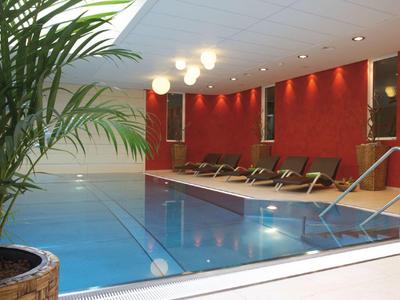 Innenpool mit roten Wänden, Liegestühlen und einer großen Topfpflanze rechts.