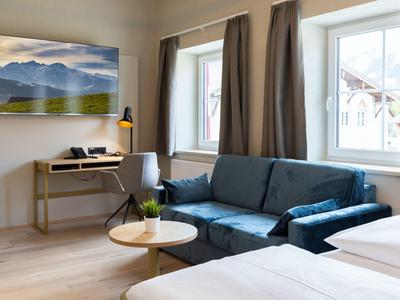Modernes Hotelzimmer mit blauem Sofa, Schreibtisch, großem Fenster und Doppelbett.
