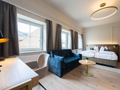 Helles Hotelzimmer mit Doppelbett, blauem Sofa, Schreibtisch und großen Fenstern.