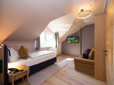 Gemütliches Hotelzimmer unter dem Dach mit Einzelbett, Sofa und hellem Holzmöbeln.