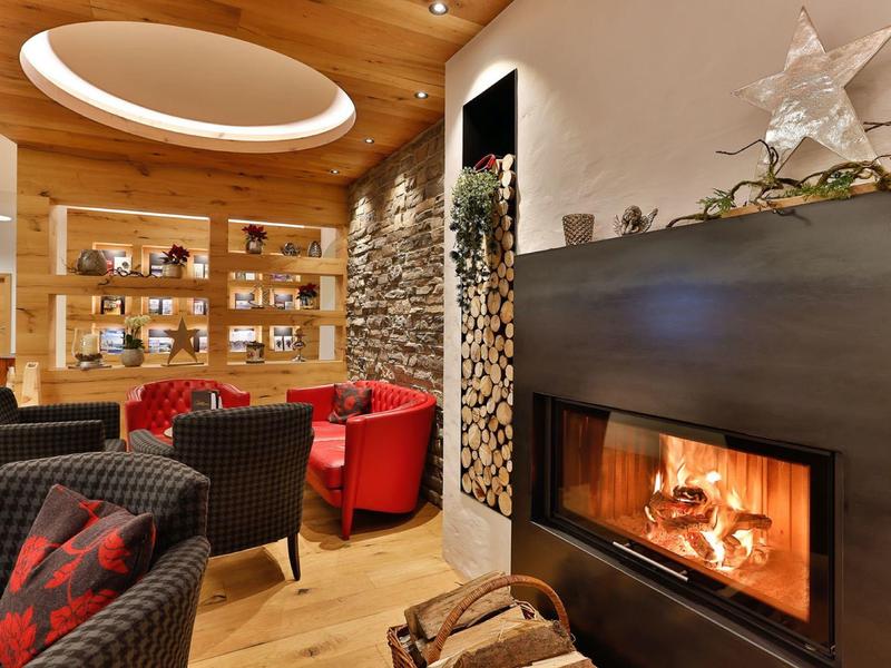 Gemütlicher Hotel-Loungebereich mit Kamin, Holzregalen und bequemen Sesseln in Rot und Schwarz.
