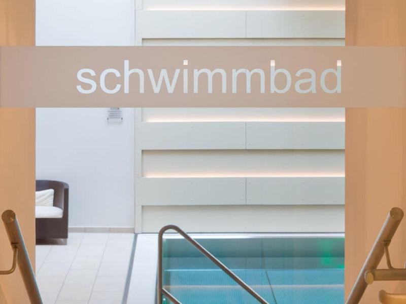 Innenbereich eines Schwimmbads mit Pool, Treppen und weißen Wänden.