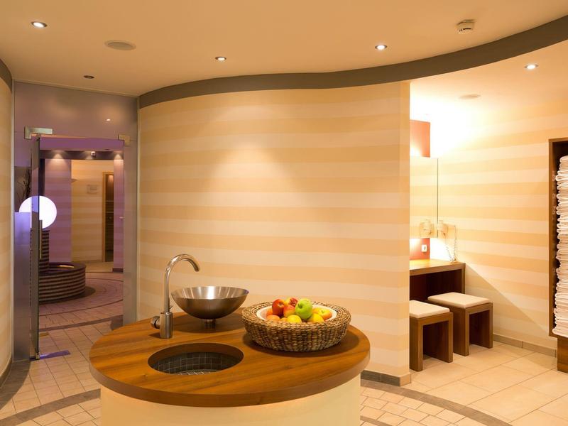 Moderner Wellnessraum mit runder Holzbank, Obstkorb und Handtüchern an der Wand.